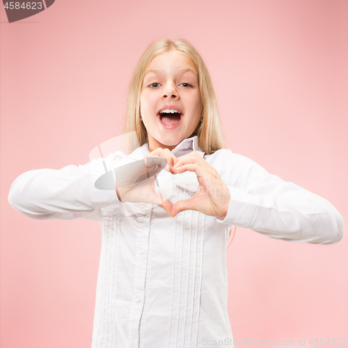 Image of Beautiful smiling teen girl makes the shape of a heart with her hands on the pink background.