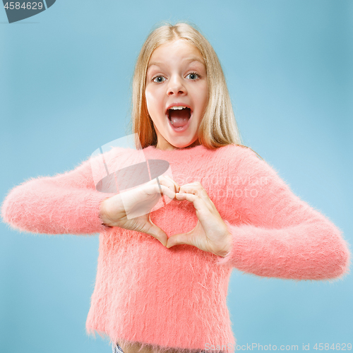 Image of Beautiful smiling teen girl makes the shape of a heart with her hands on the blue background.