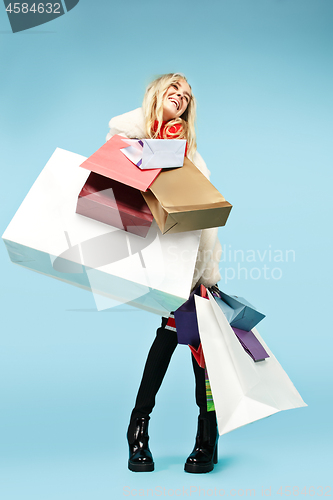 Image of Full length portrait of a beautiful smiling woman walking with colorful shopping bags isolated over blue background