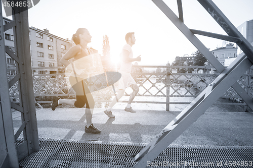 Image of young couple jogging across the bridge in the city