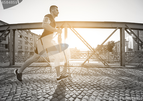 Image of man jogging across the bridge at sunny morning