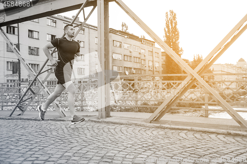 Image of man jogging across the bridge at sunny morning