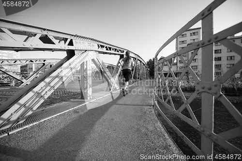 Image of woman jogging across the bridge at sunny morning