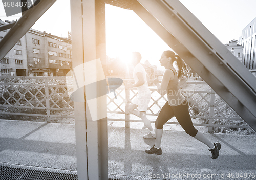 Image of young couple jogging across the bridge in the city