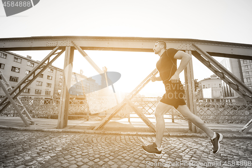 Image of man jogging across the bridge at sunny morning