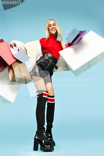 Image of Full length portrait of a beautiful smiling woman walking with colorful shopping bags isolated over blue background