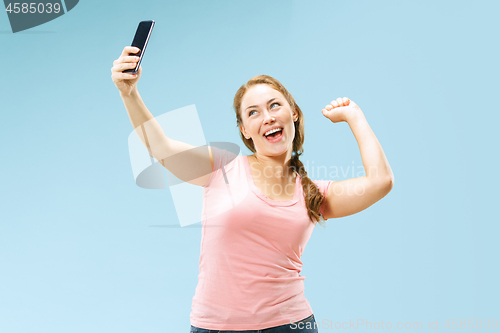 Image of Portrait of a happy smiling casual girl showing blank screen mobile phone isolated over blue background