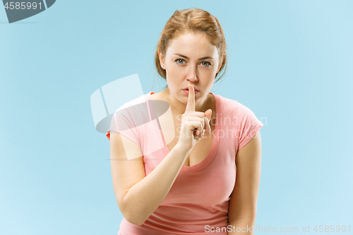 Image of The young woman whispering a secret behind her hand over blue background