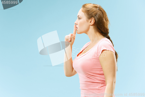 Image of The young woman whispering a secret behind her hand over blue background