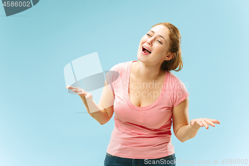 Image of Beautiful female half-length portrait isolated on blue studio backgroud. The young emotional surprised woman