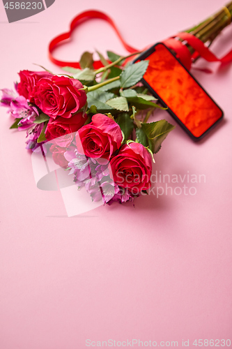 Image of Pink roses bouquet with hart shaped bow and mobile phone with copy space screen