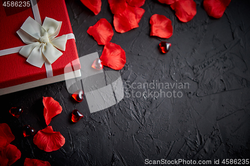 Image of Gift box on black stone table. Romantic holiday background with rose petals