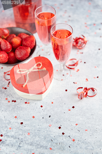 Image of Bottle of rose champagne, glasses with fresh strawberries and heart shaped gift