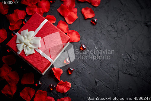 Image of Gift box on black stone table. Romantic holiday background with rose petals