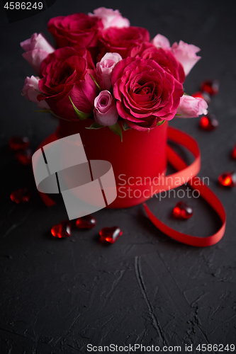 Image of Pink roses bouquet packed in red box and placed on black stone background