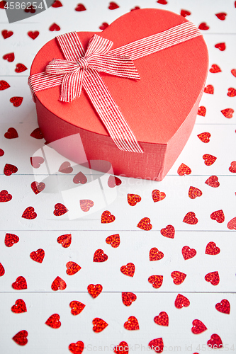 Image of Boxed gift placed on heart shaped red sequins on white wooden table