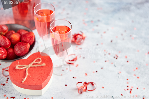 Image of Bottle of rose champagne, glasses with fresh strawberries and heart shaped gift