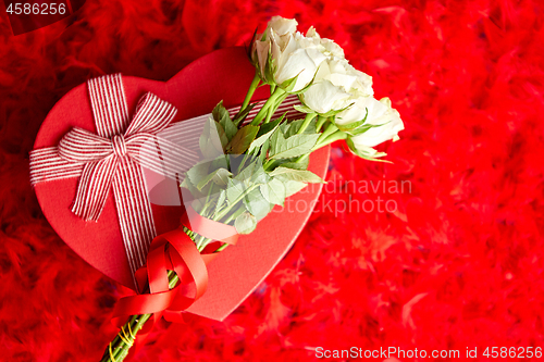 Image of Heart shaped boxed gift, placed on red feathers background