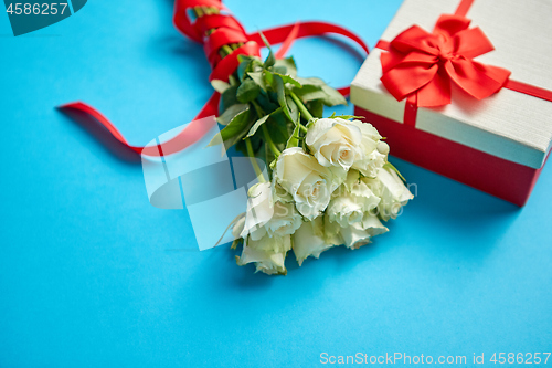 Image of Bouquet of white roses with red bow on blue background. Boxed gift on side