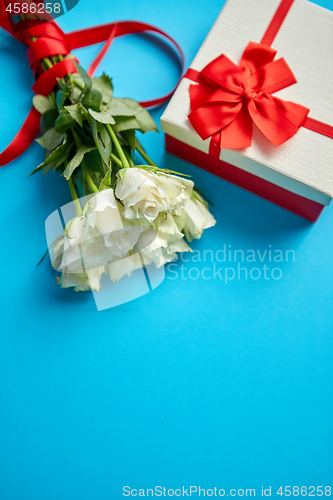 Image of Bouquet of white roses with red bow on blue background. Boxed gift on side