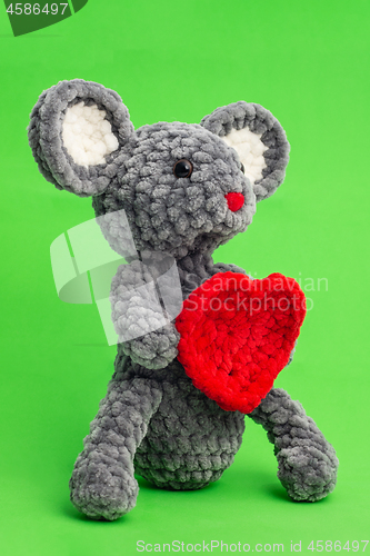 Image of Grey knitted mouse with a heart in hand on a green background, side view