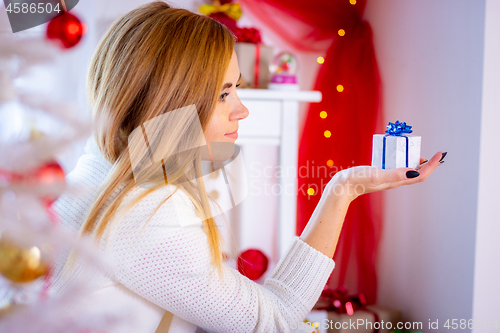 Image of Young girl sits with a small Christmas gift at the Christmas tree, close-up