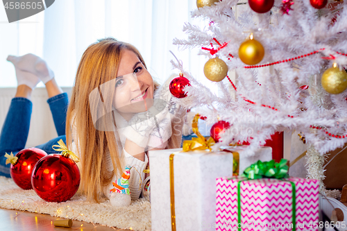 Image of A young girl lies at the Christmas tree and looks happy in the frame