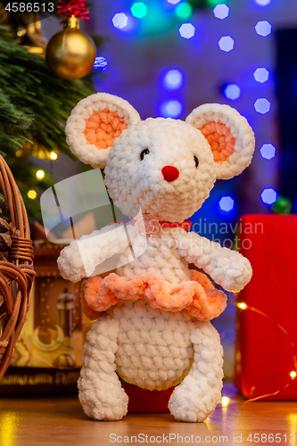 Image of Knitted toy white mouse in a sunface under a Christmas tree