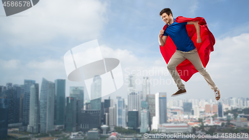 Image of man in red superhero cape flying in air over city