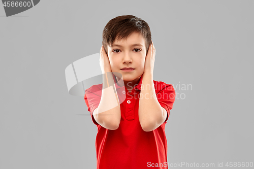 Image of boy in red t-shirt closing ears by hands