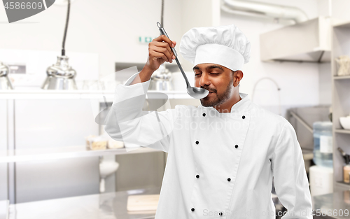 Image of happy indian chef tasting food by ladle at kitchen