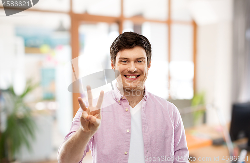 Image of young man showing three fingers over office room