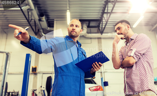 Image of auto mechanic with clipboard and man at car shop