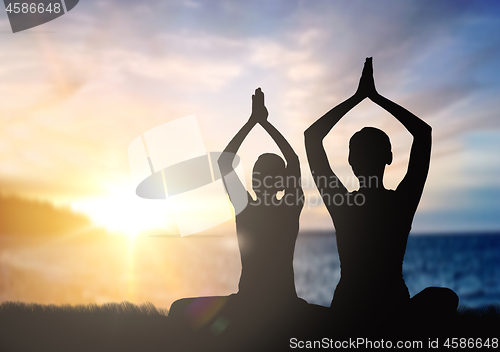 Image of couple doing yoga in lotus pose over sunset