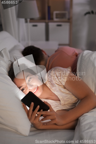 Image of woman using smartphone while boyfriend is sleeping