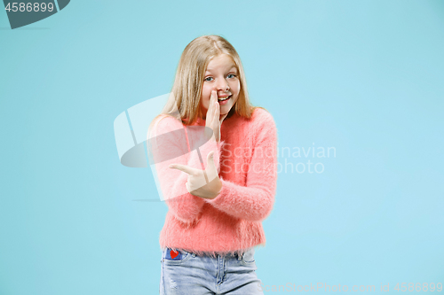 Image of The young teen girl whispering a secret behind her hand over blue background