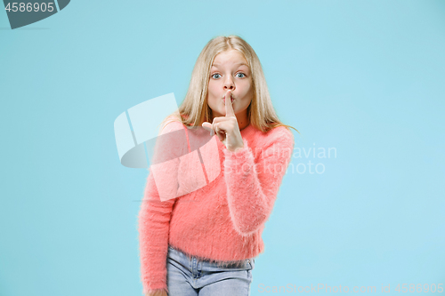 Image of The young teen girl whispering a secret behind her hand over blue background