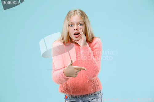 Image of The young teen girl whispering a secret behind her hand over blue background