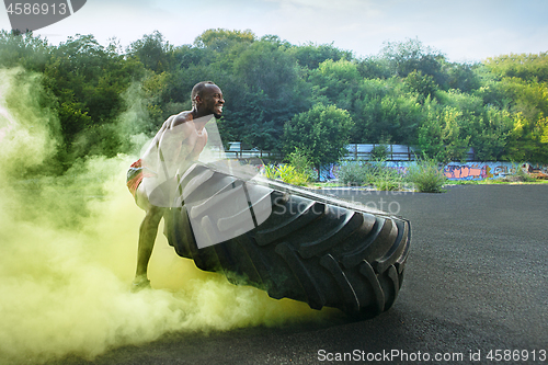 Image of Handsome muscular man flipping big tire outdoor.