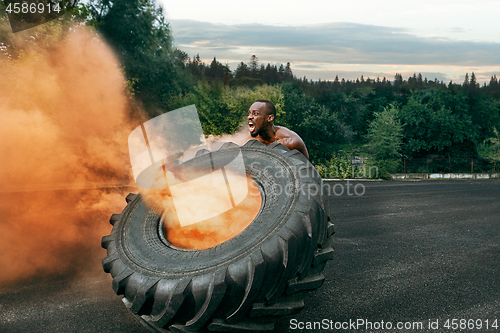 Image of Handsome muscular man flipping big tire outdoor.