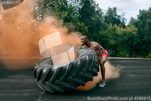 Image of Handsome muscular man flipping big tire outdoor.