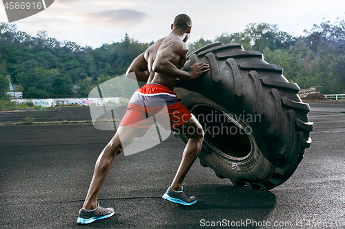 Image of Handsome muscular man flipping big tire outdoor.