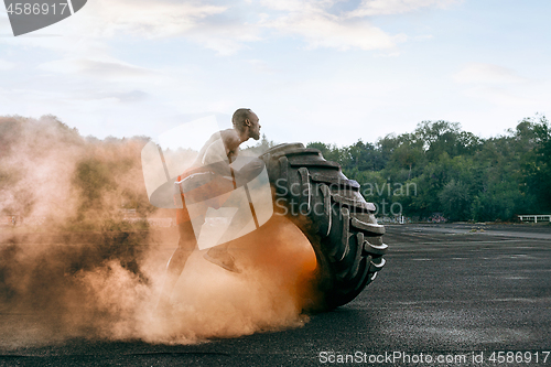 Image of Handsome muscular man flipping big tire outdoor.