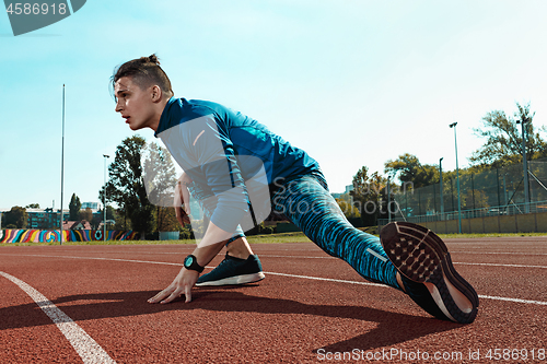 Image of Man runner stretching legs preparing for run training on stadium tracks doing warm-up