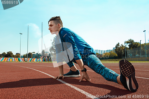 Image of Man runner stretching legs preparing for run training on stadium tracks doing warm-up