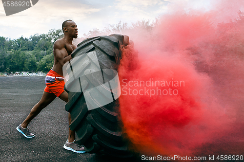 Image of Handsome muscular man flipping big tire outdoor.