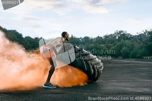 Image of Handsome muscular man flipping big tire outdoor.