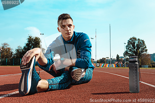 Image of Man runner stretching legs preparing for run training on stadium tracks doing warm-up