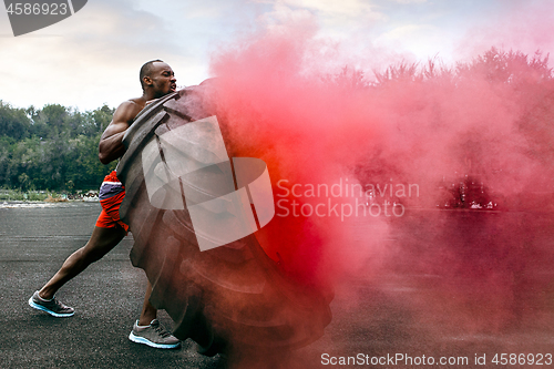 Image of Handsome muscular man flipping big tire outdoor.