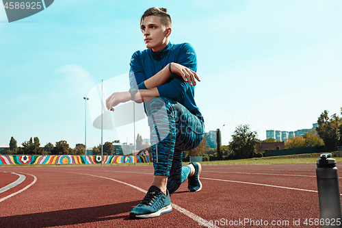 Image of Man runner stretching legs preparing for run training on stadium tracks doing warm-up